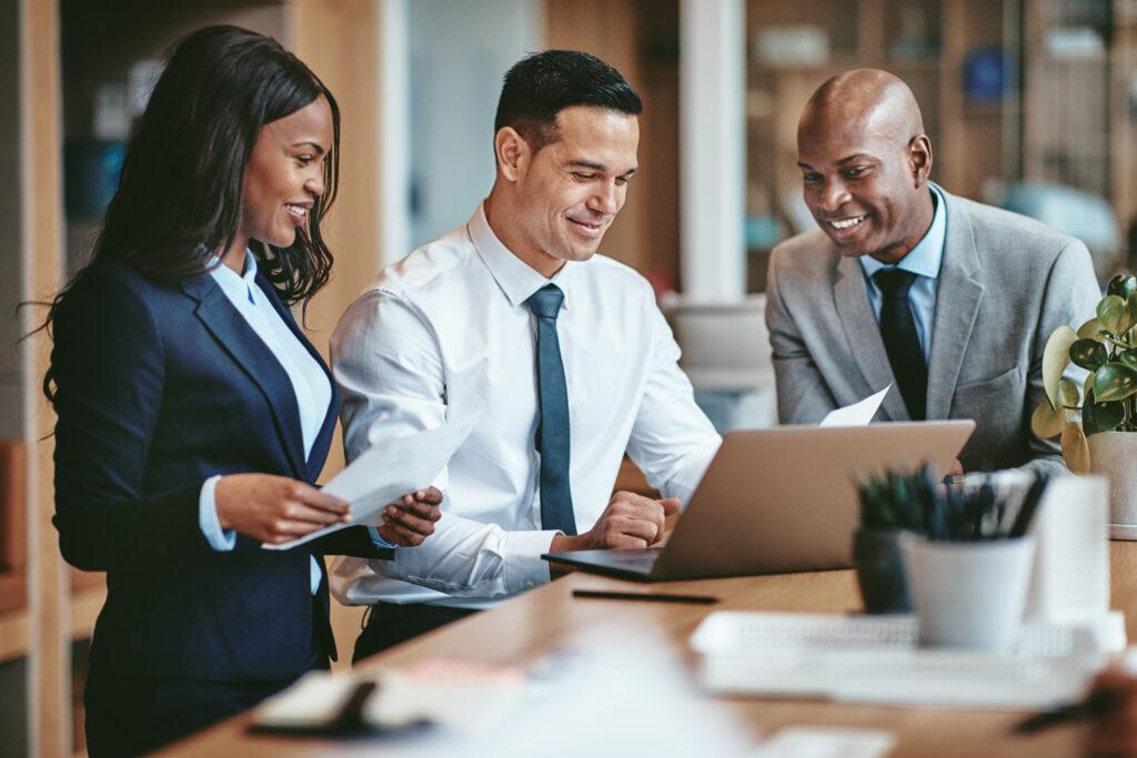 A woman and two men examine a laptop. 