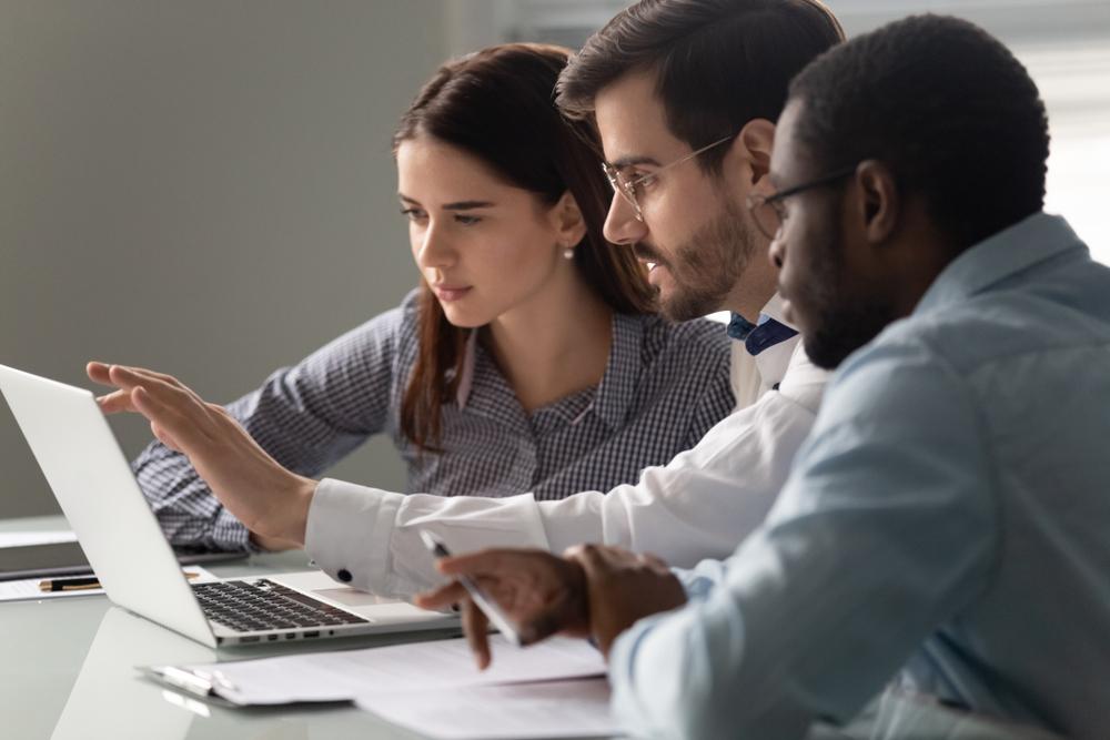 A woman and two men look at a laptop as they address an information technology issue. 